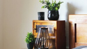 A neatly made bed with a white pillow and a gray blanket, a wooden nightstand with a small potted plant, a black vase, and a decorative metal lamp. - Vineyard cottage Ranč pri Hanzeku (Videm)