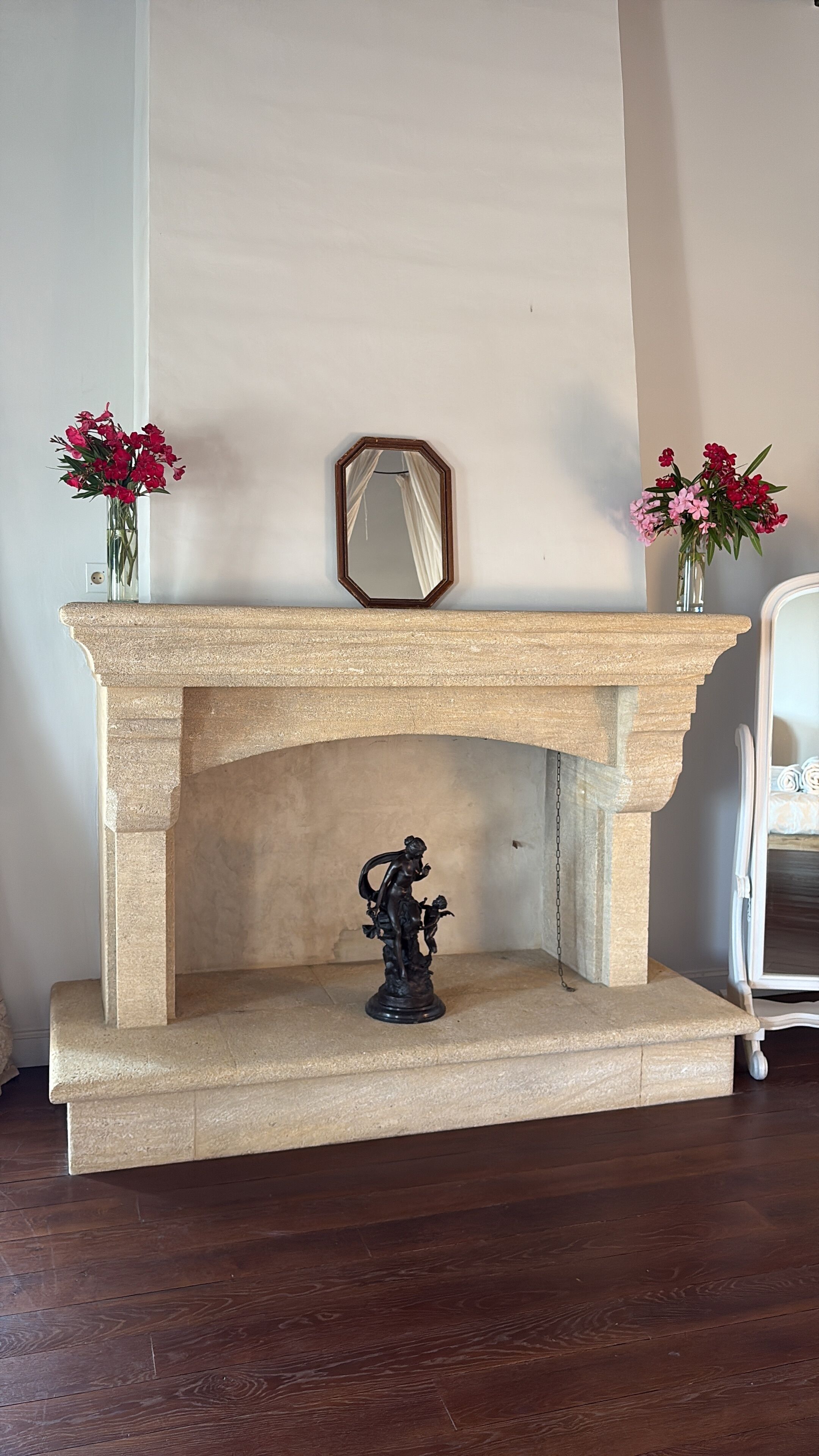 Una chimenea de piedra con una estatua decorativa debajo, flanqueada por dos jarrones de flores.