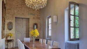 A dining room with a large wooden table, white chairs, a chandelier, stone walls, and a view through a window. - LUXURY CHATEAU FOR RENT UZES PROVENCE (Saint-Maximin)