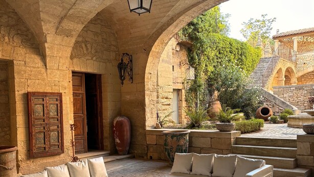 An outdoor seating area with stone arches, white sofas, and a table set for dining. - LUXURY CHATEAU FOR RENT UZES PROVENCE (Saint-Maximin)