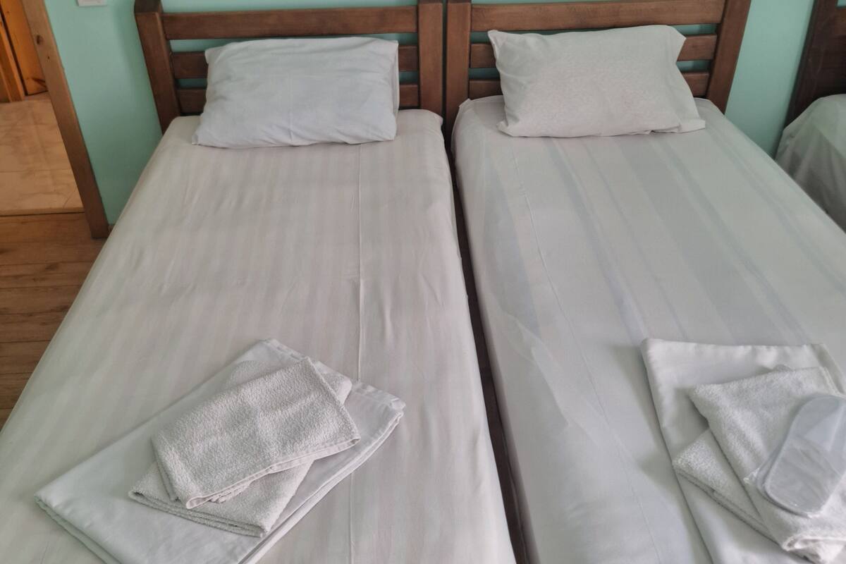 Two single beds with wooden headboards and white linens, including folded towels on each bed.