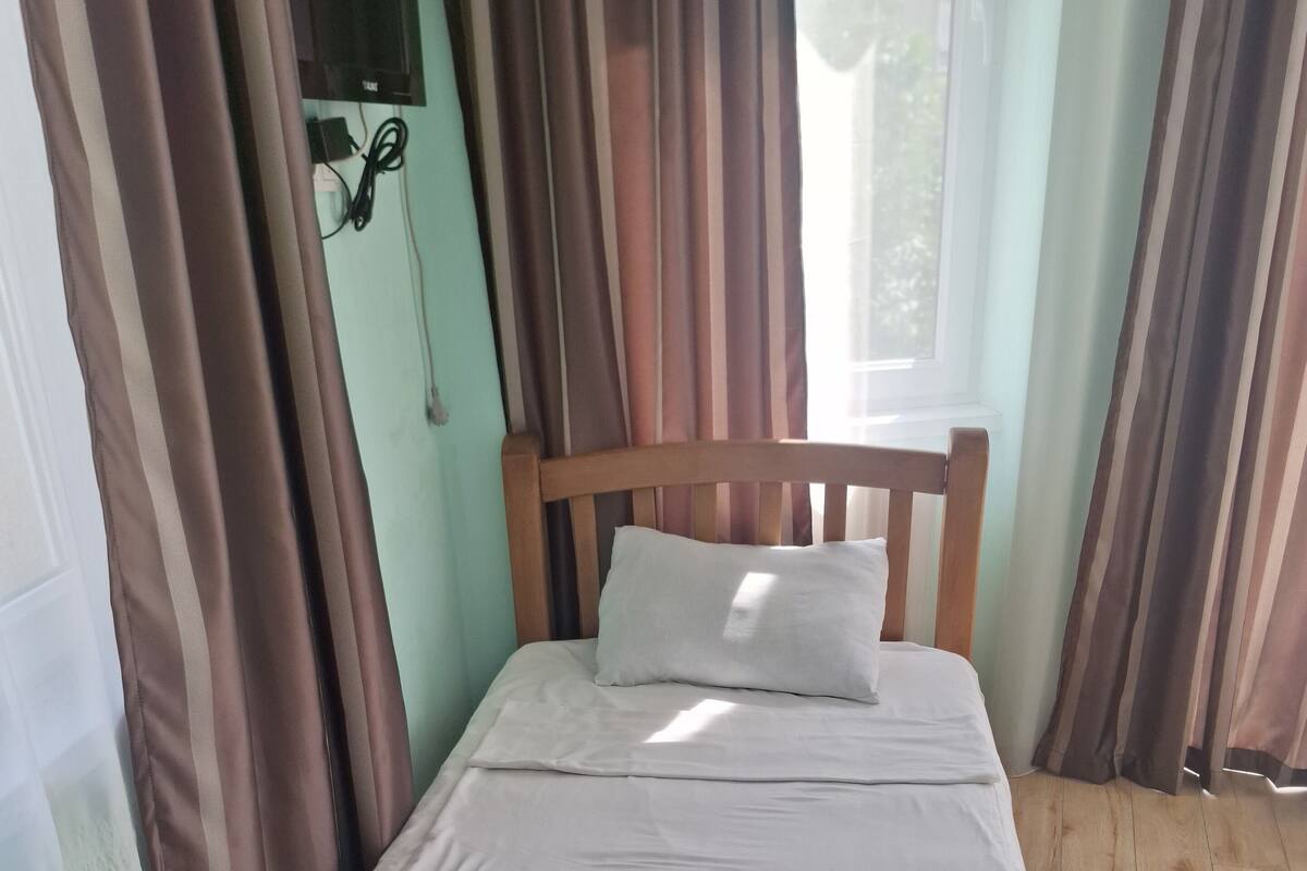A single bed with a wooden headboard, white bedding, and a folded white towel.