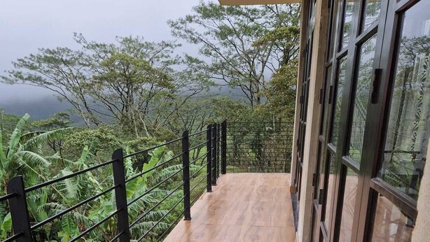 Una terraza de madera con barandas metálicas, con vistas a un jardín exuberante y colinas distantes.