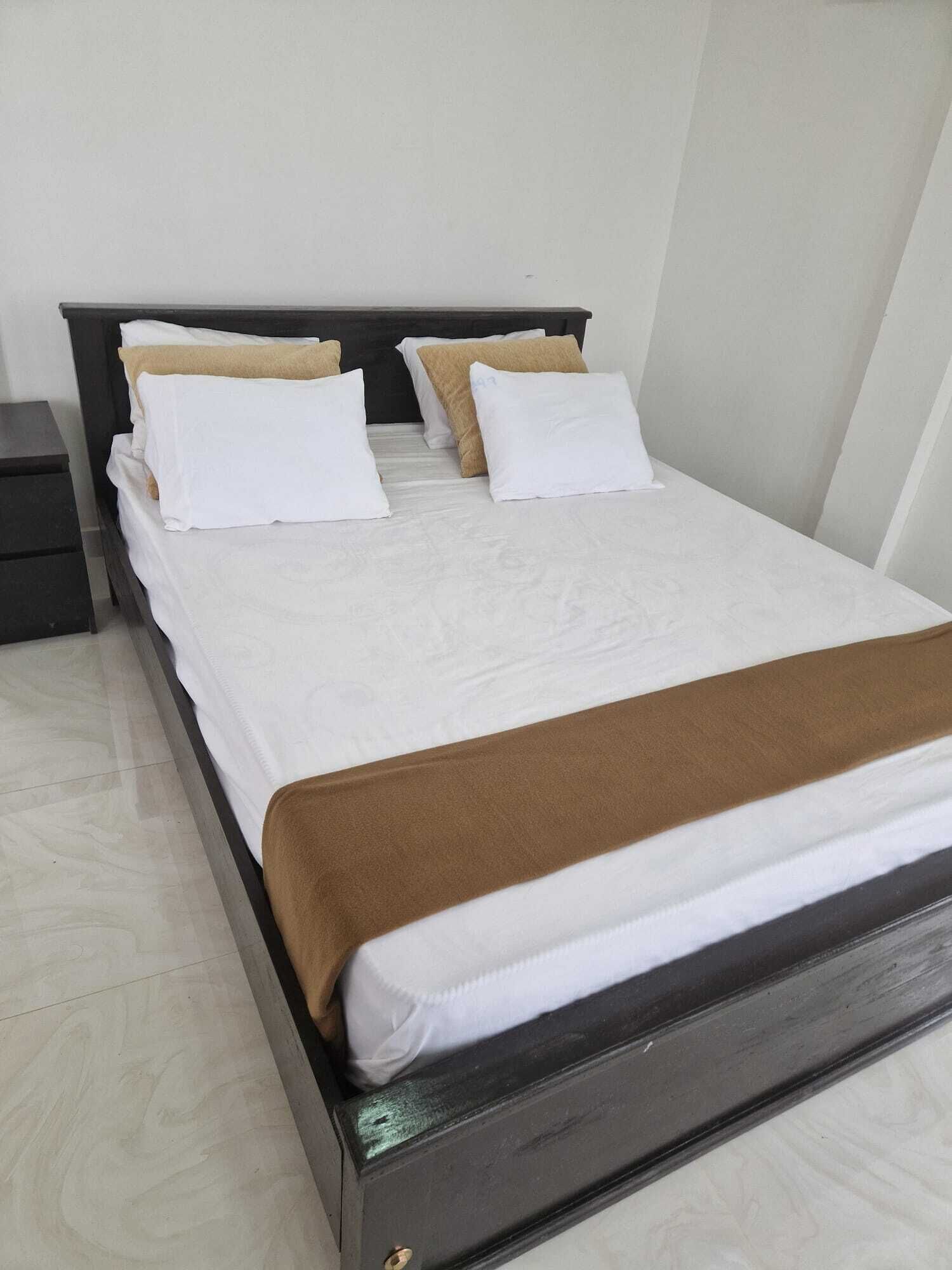 A neatly made bed with white and brown bedding, a dark wooden headboard, and a small bedside table.