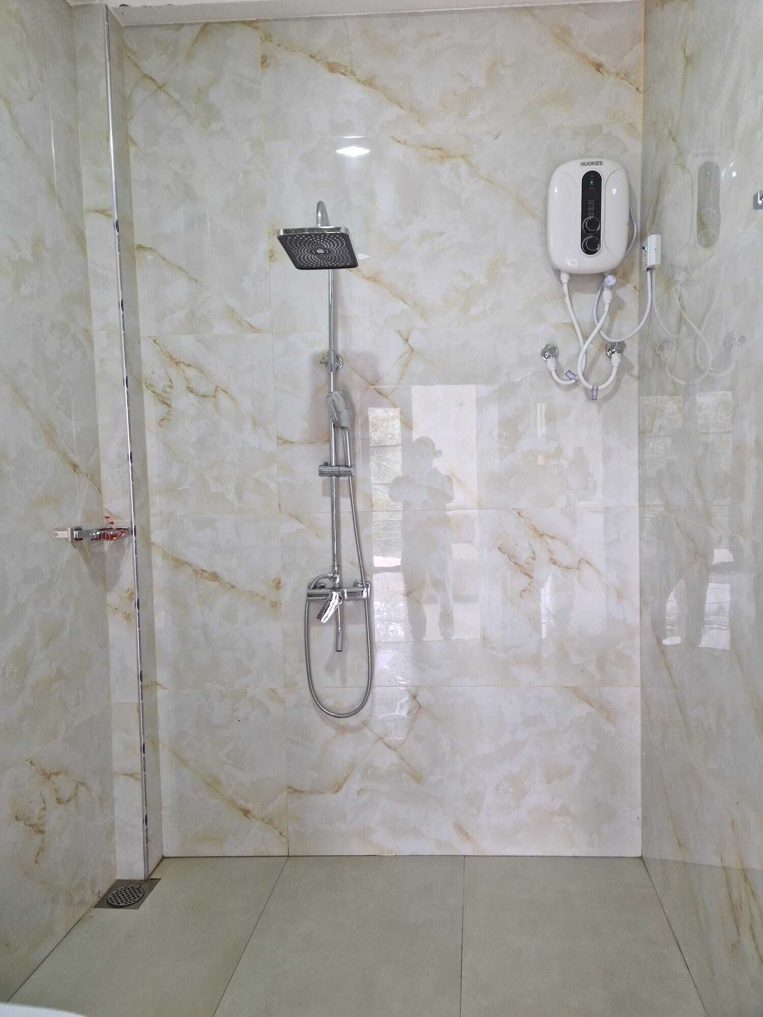 Un baño con pared de mármol, cabezal de ducha de mano y panel de control en la pared.