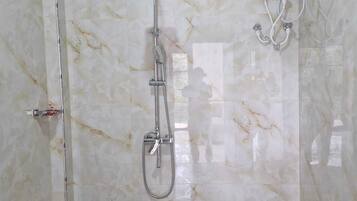 Un baño con pared de mármol, cabezal de ducha de mano y panel de control en la pared.