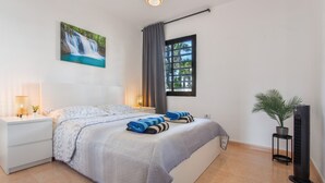 A bedroom with a bed, a nightstand, a lamp, a window with curtains, a potted plant, and a wall-mounted TV. - Coral Bliss Apartment with Shared Pool, Private Terrace, and Wi-Fi (Corralejo)