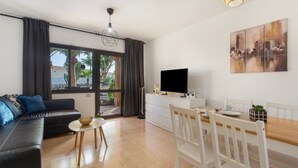 A modern living room with a sofa, dining table, chairs, a TV, and a cityscape painting. - Coral Bliss Apartment with Shared Pool, Private Terrace, and Wi-Fi (Corralejo)