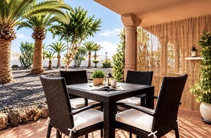 En udendørs terrasse med fletmøbler, et bord og stole.