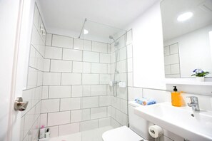 Une salle de bain moderne avec une douche à l’italienne en verre, des carreaux blancs, un lavabo blanc avec un miroir et des articles de toilette.