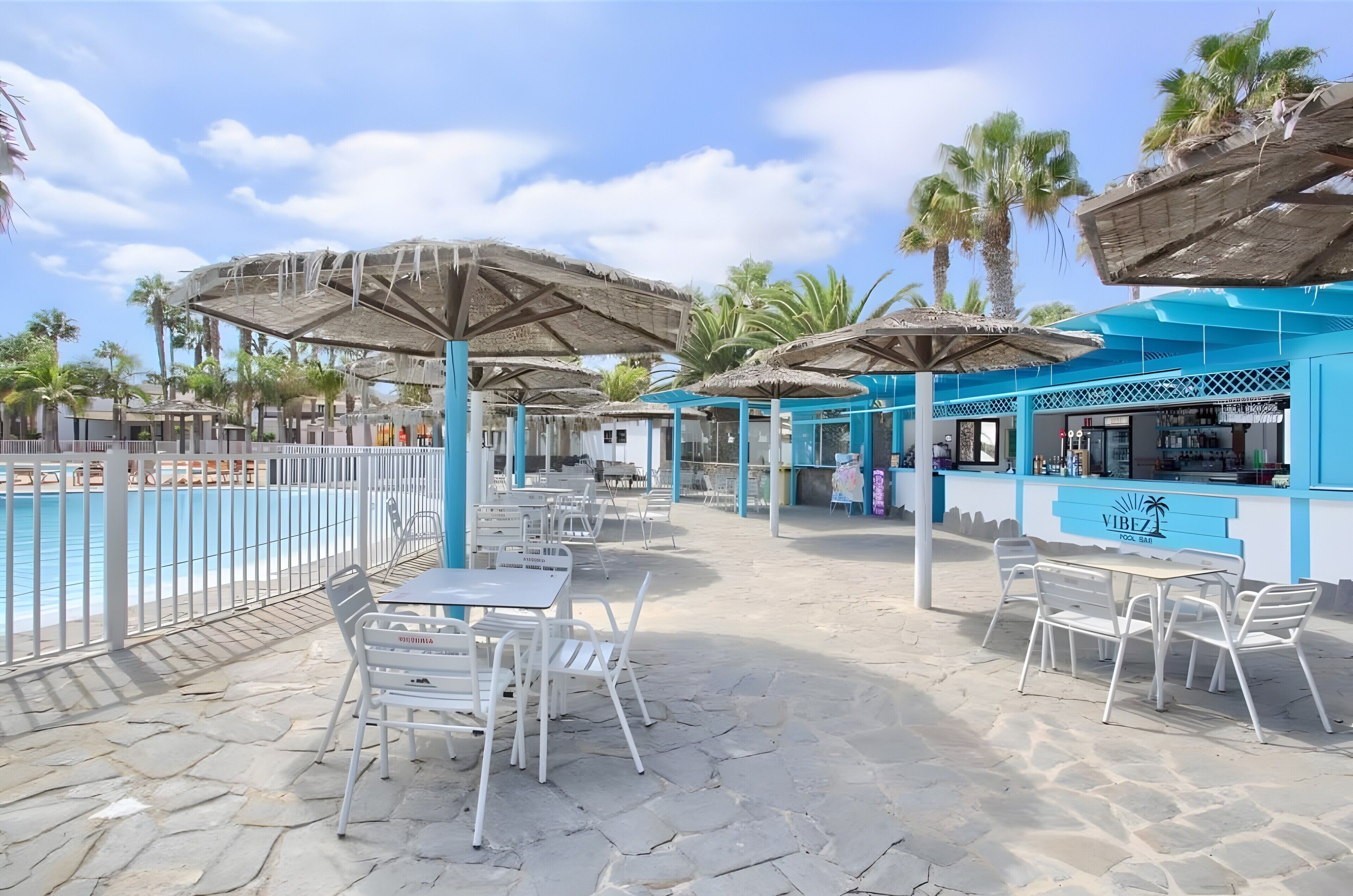 Un espace aménagé au bord de la piscine, avec des sièges et des parasols, un bar et une piscine.