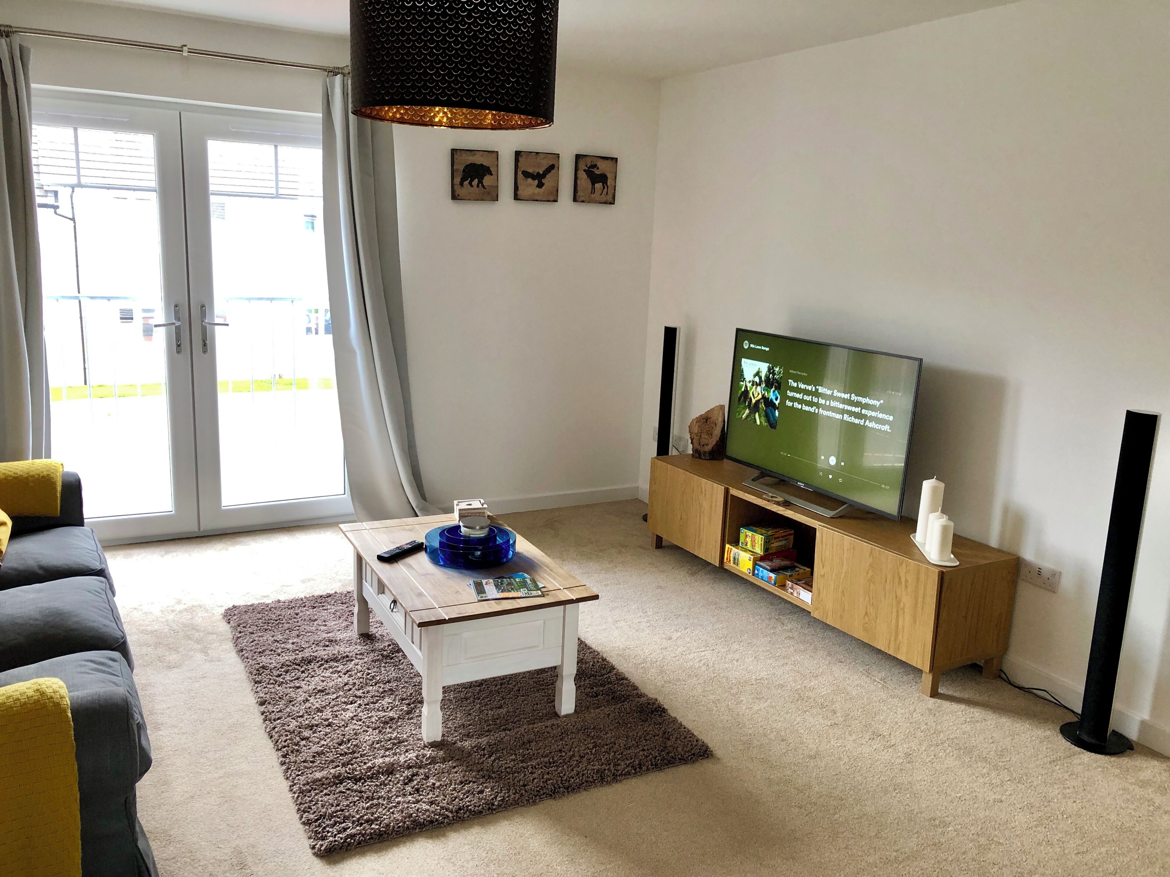 A living room with a sofa, a coffee table, a TV on a wooden stand, and a large window with curtains.