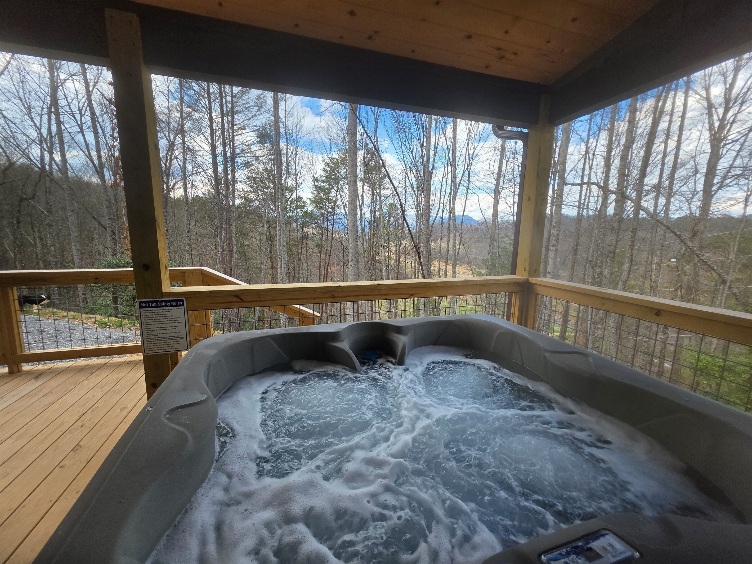 A hot tub with a wooden deck and a view of a forested area.