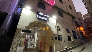 Exterior del Hotel Al Sukariya con un diseño moderno, destacando un llamativo letrero de neón rosado y una escalera que conduce a la entrada.