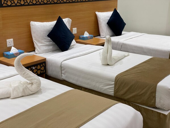Habitación de hotel con dos camas, cada una con ropa de cama blanca y almohadas azules. Hay una caja de pañuelos en la mesita de noche, y una toalla sobre la cama.