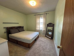 Ein Schlafzimmer mit einem Einzelbett, einem Holzkopfstück, einem kleinen Nachttisch, einem Spiegel und einer Tür.