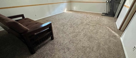A room with a brown upholstered bench, carpeted floor, and a window with blinds.