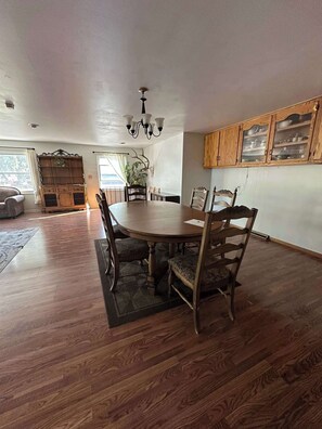 Un vaste espace dédié à la salle à manger, avec une table et des chaises en bois, un lustre et des meubles de rangement en bois dotés de portes en verre.