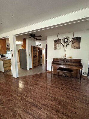Un vaste salon doté d’un plancher en bois franc, d’un piano et d’un ventilateur de plafond.