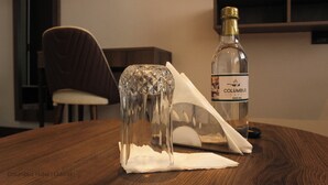 A bottle of Columbus Cafe 500 ML on a wooden table with a clear glass object and a napkin. - Columbus Hotel Eldoret (Eldoret)