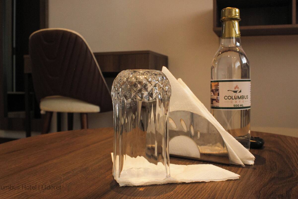 Una botella de Café Columbus de 500 ml sobre una mesa de madera, con un objeto de vidrio transparente y una servilleta.