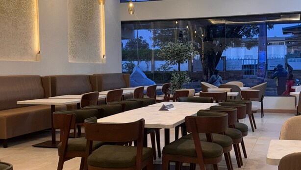 A modern restaurant with a mix of booth and table seating, large windows, and a view of the outdoors. - Columbus Hotel Eldoret (Eldoret)