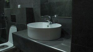 A bathroom with a round white sink, a mirror, and dark tiles. - Columbus Hotel Eldoret (Eldoret)