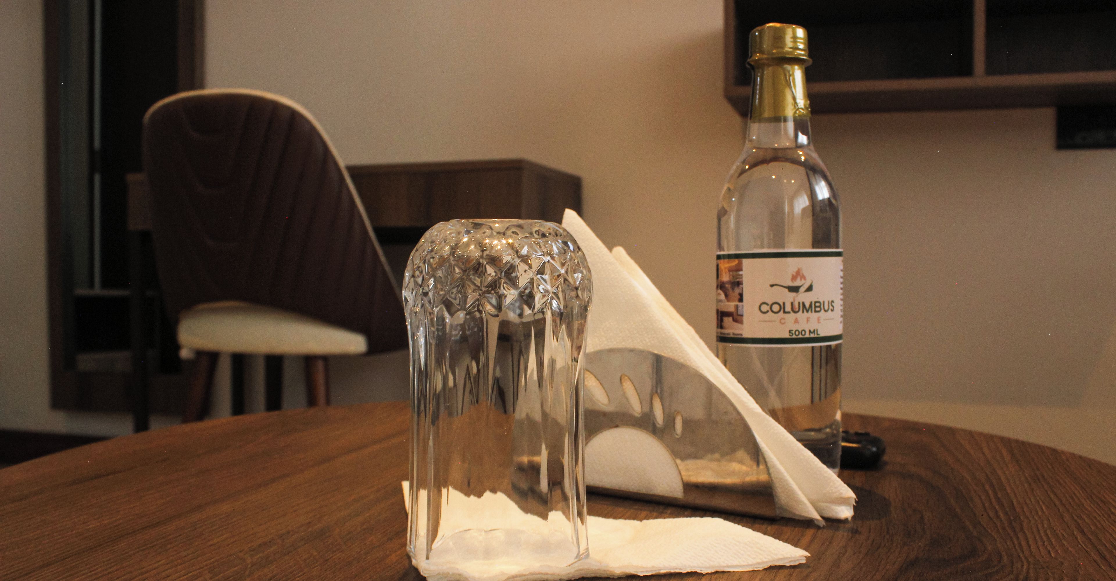 Eine Flasche Columbus Cafe mit 500 ml auf einem Holztisch, zusammen mit einem klaren Glasobjekt und einer Serviette.