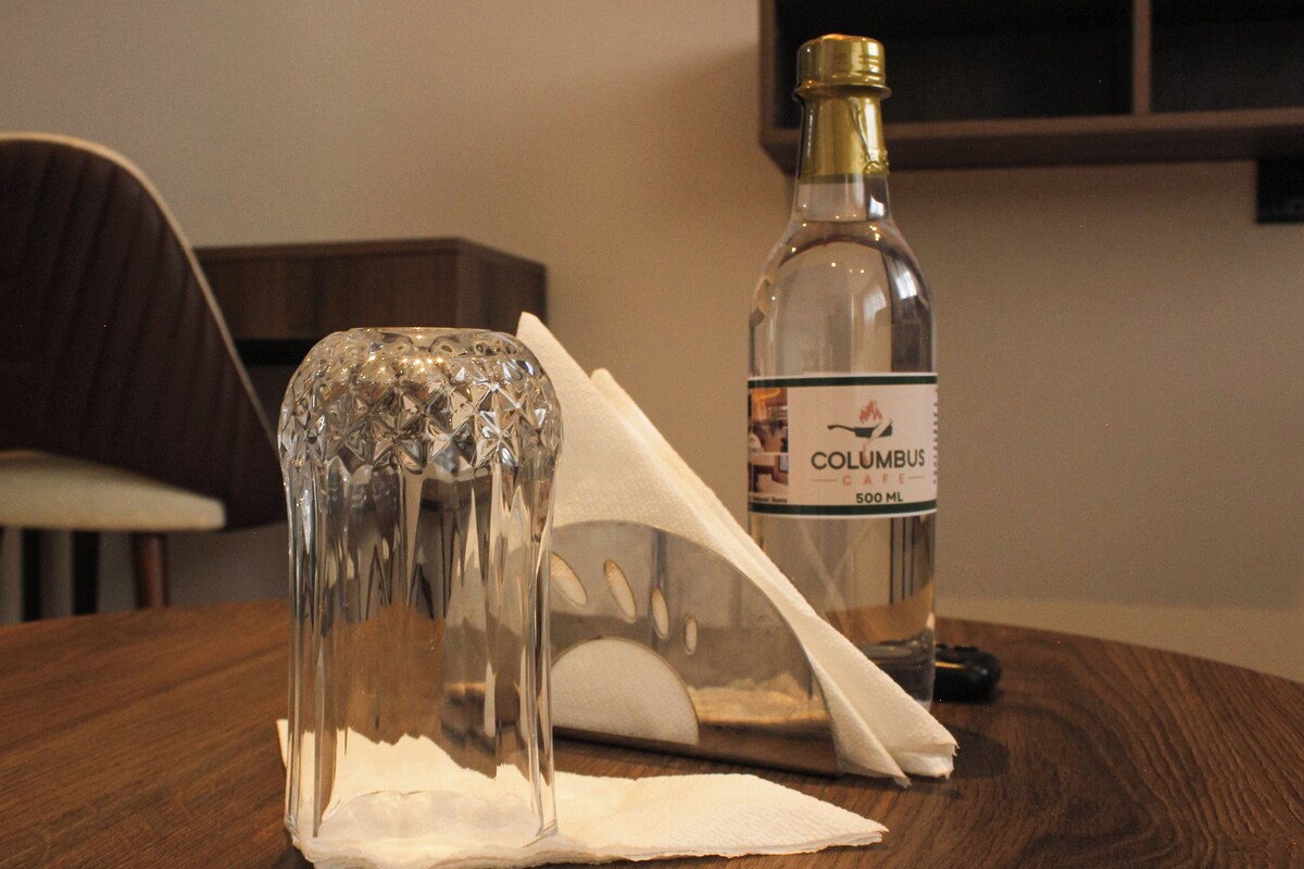 Eine Flasche Columbus Cafe mit 500 ml auf einem Holztisch, zusammen mit einem klaren Glasobjekt und einer Serviette.