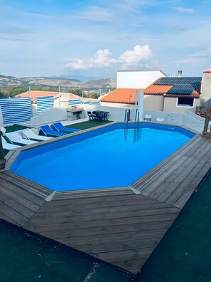 A rooftop swimming pool with a wooden deck, lounge chairs, and a table. - Apartment 'Casa rinascita' with Private Pool (Nulvi)
