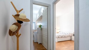 A room with a bed, a wooden floor, a white wall, and a doorway leading to a kitchen area. - Casa Rinascita with Private Pool (Nulvi)