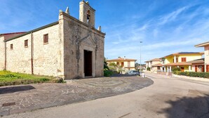 A stone building with a bell tower, a paved area, and adjacent houses. - Casa Rinascita with Private Pool (Nulvi)