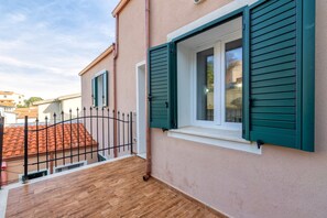 Ein Gebäude mit einem Balkon, einem Fenster mit grünen Rollläden und einem Metallzaun.