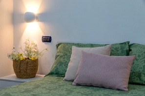 Ein Bett mit grüner Bettwäsche, einem violetten Kopfkissen und einem Korbwäsche mit Blumen.