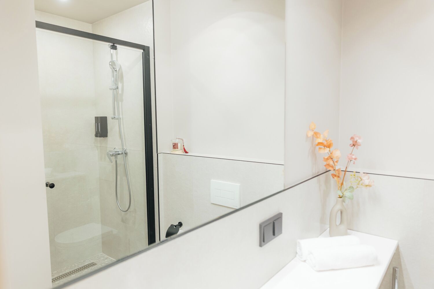 A modern bathroom with a glass-enclosed shower, a white sink, and a vase with flowers.