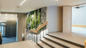 A modern staircase with a wooden handrail, a wall with green plants, and a door at the top. - Aparthotel Aurum (Rīga)
