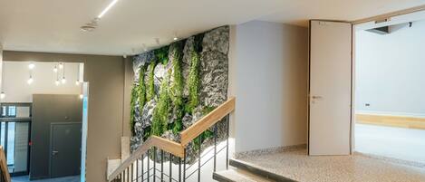 Un escalier moderne avec une rampe en bois, un mur orné de plantes vertes et une porte en haut.