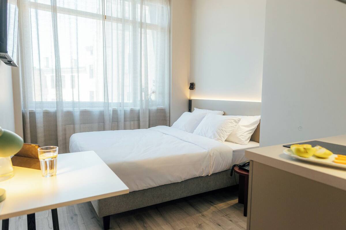 A modern hotel room with a bed, bedside table, and a small desk with a plate of fruit.