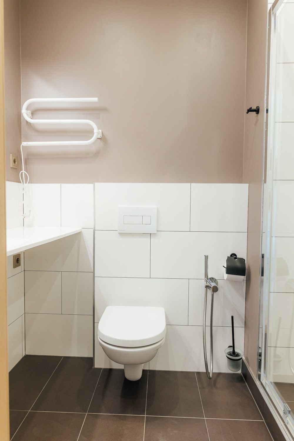 A bathroom with a white toilet, a towel rack, a shower, and a hand dryer.