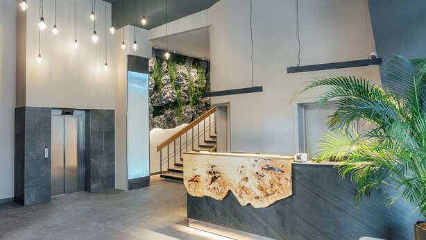A modern reception area with a stone wall, a wooden reception desk, and a staircase leading to an upper floor. - Aparthotel Aurum (Rīga)