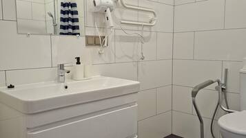 Et moderne badeværelse med hvid kommode, spejl, håndklæderække og toilet.
