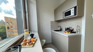 A compact kitchen with a microwave, sink, and a window overlooking a cityscape. - Aparthotel Aurum (Rīga)