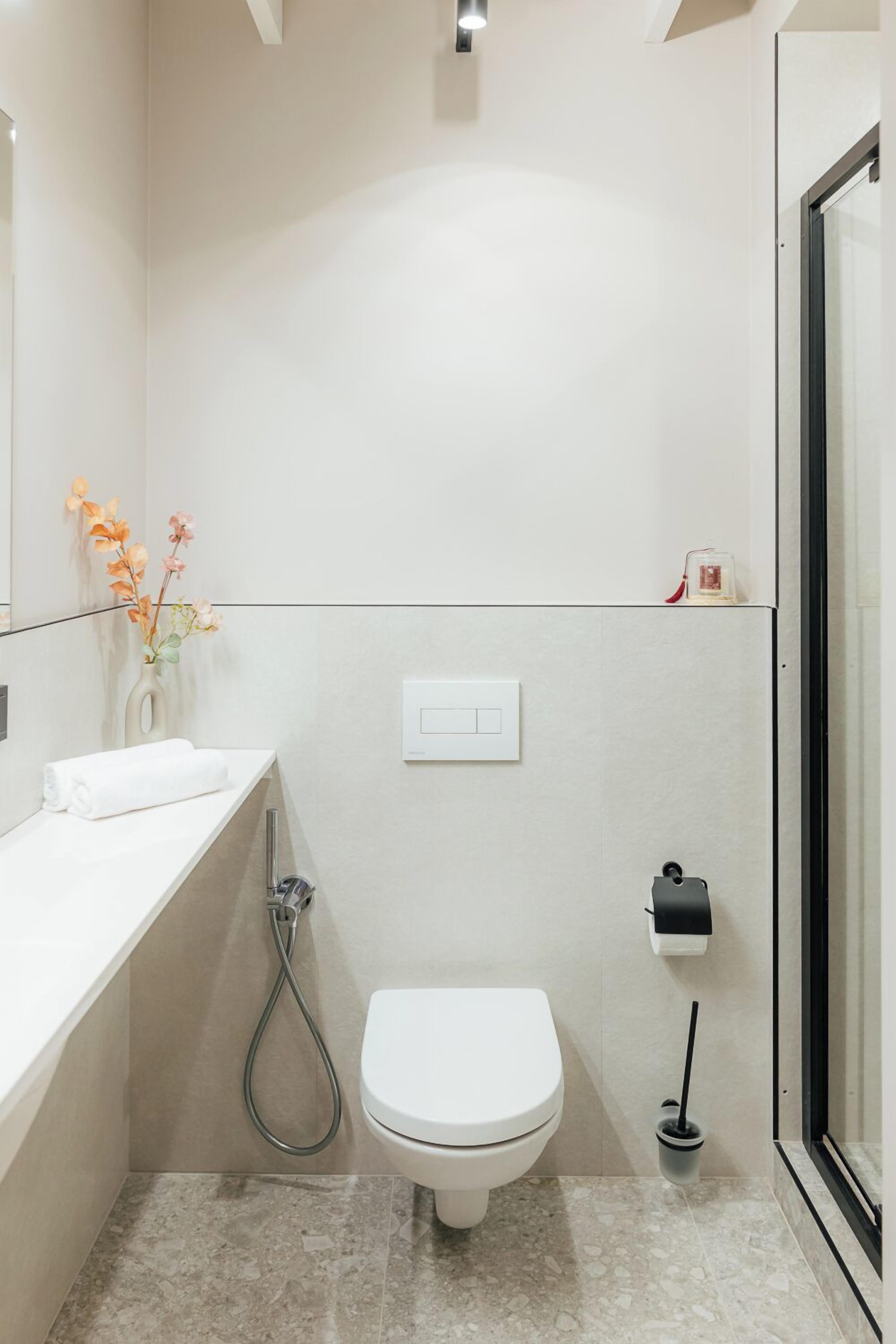 A modern bathroom with a white toilet, a shower, a towel rack, and a toilet paper holder.