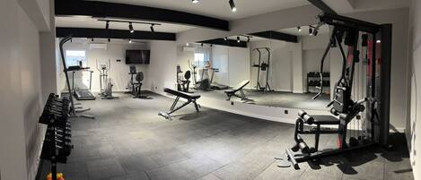 A gym with various exercise equipment, a television, and a large mirror.
