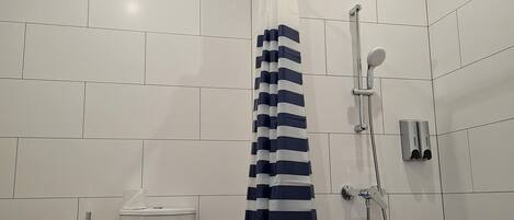 Ett modernt badrum med vita kakelplattor, en vit toalett, en dusch med ett randigt duschdraperi och ett duschmunstycke som kan hållas i handen.