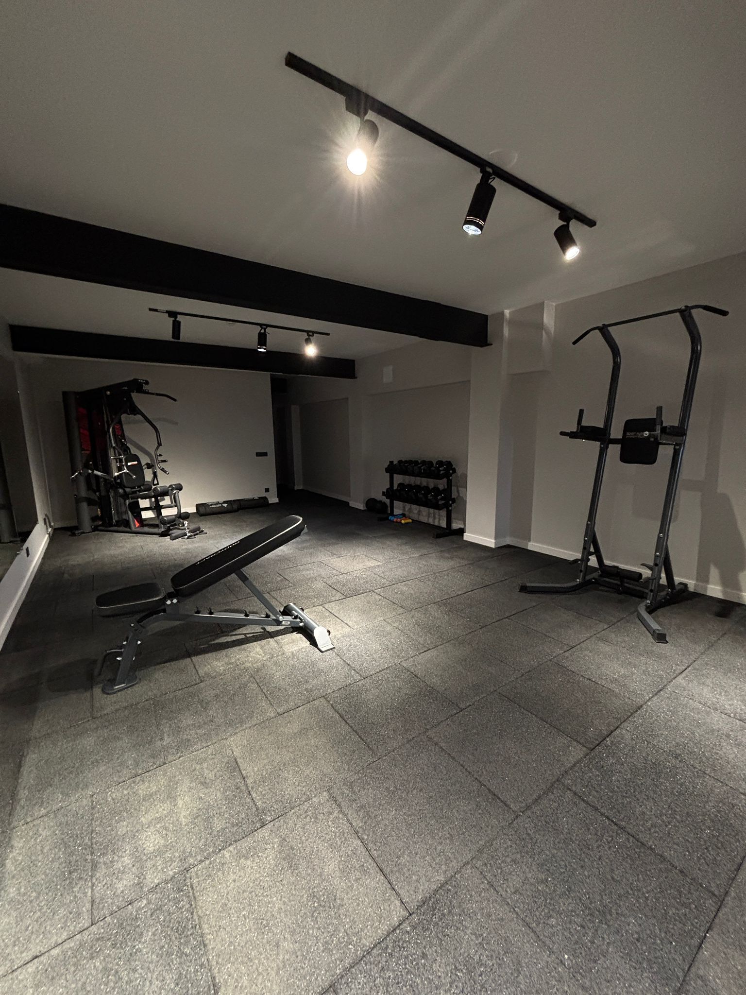 A gym with a bench press, dumbbells, and a squat rack.