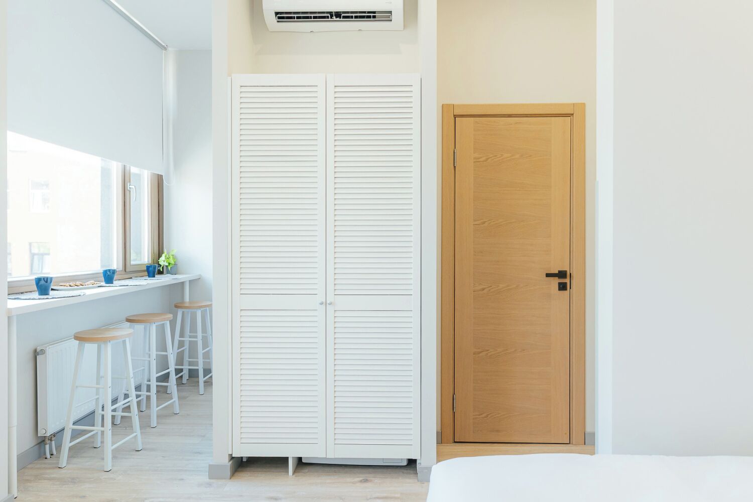 Un dormitorio con cama, una puerta de madera, un armario blanco y una ventana con vistas.