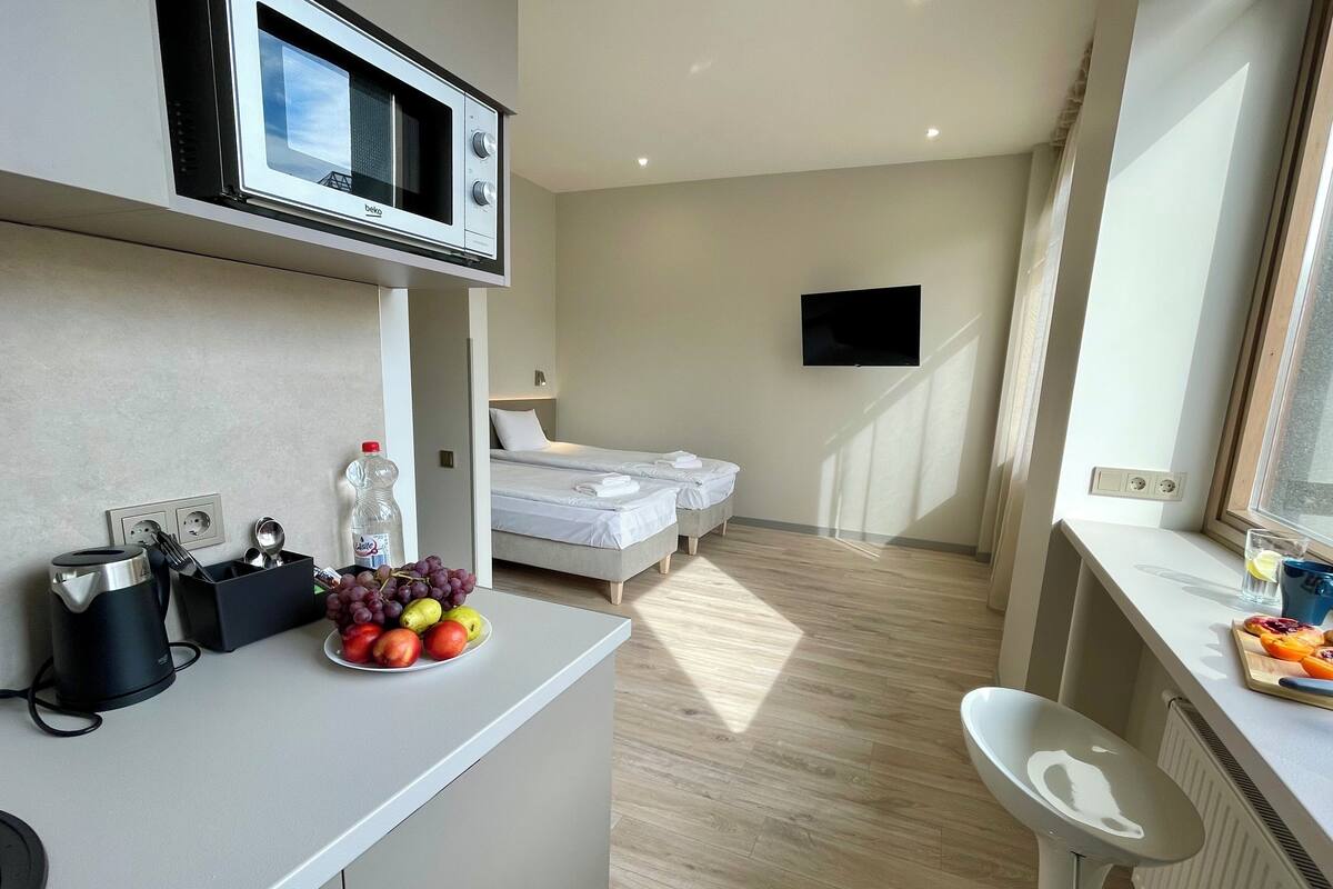 A modern hotel room with a kitchenette, a bed, a TV, and a bathroom.