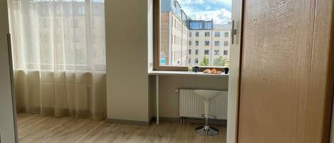 A room with a wooden floor, a window with a view of buildings, a radiator, and a door with a handle.