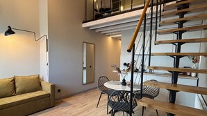 A modern loft-style apartment with a wooden staircase, a dining area, and a living room with a sofa and a lamp. - Aparthotel Aurum (Rīga)